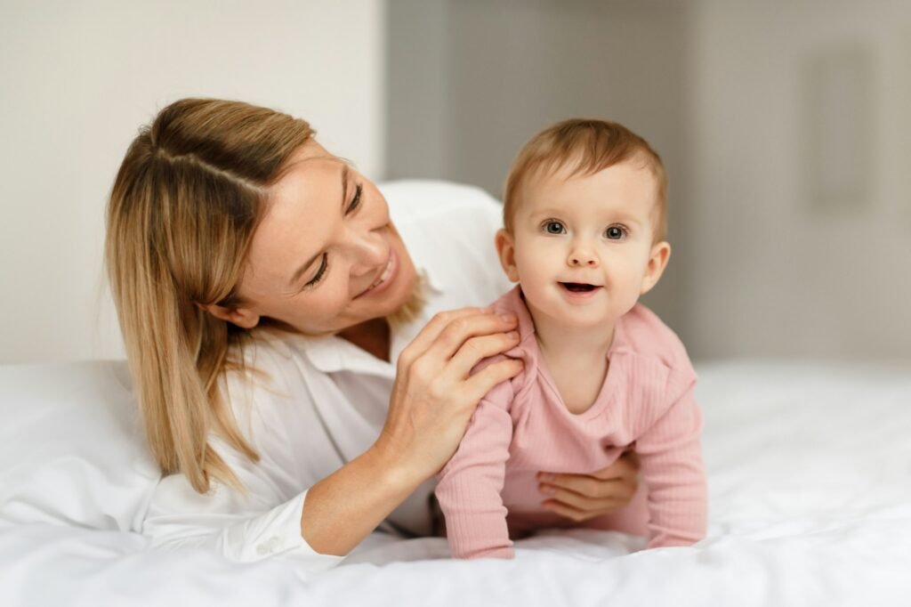 Loving mother talking and playing to her infant child girl, kid crawling and smiling at camera on